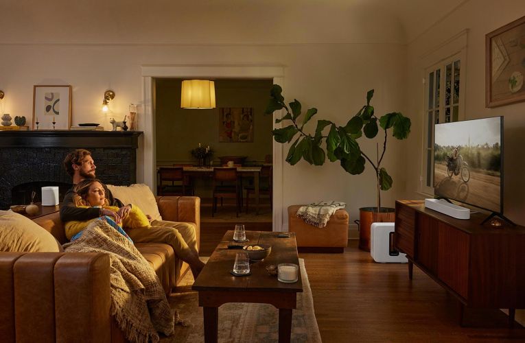 Woman and man relaxed watching TV with Sonos white speakers